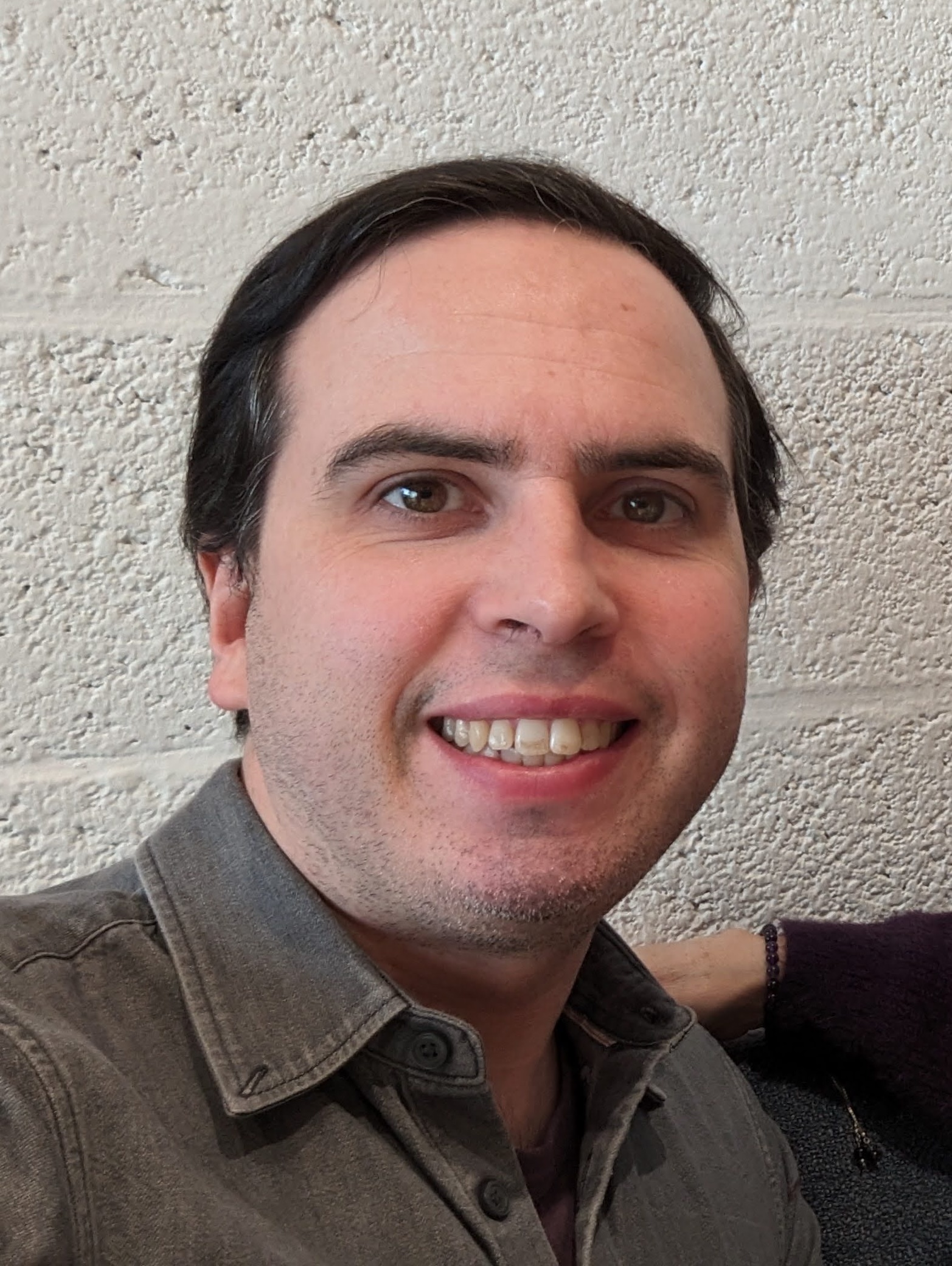 Luke wearing a grey shirt, in front of a white brick wall