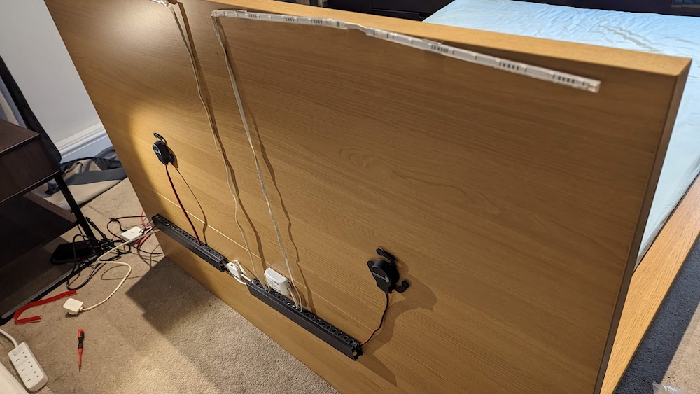 Various electronics attached to the back of a bed's headboard