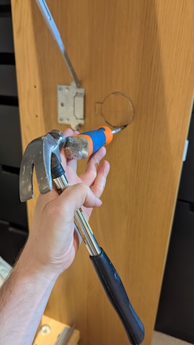 A hammer and chisel being used to cut a circle in the base of a bed